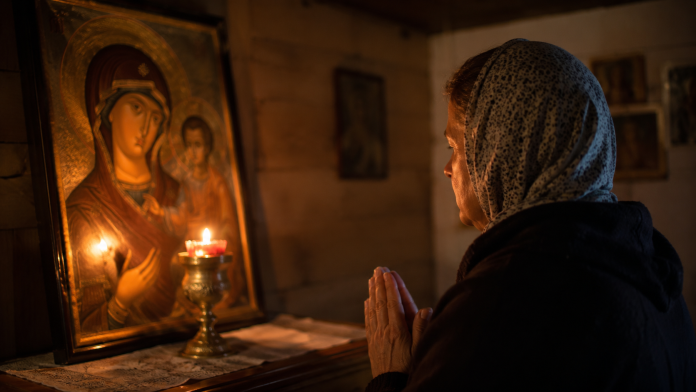 Persoană rugându-se în fața unei icoane, într-o cameră liniștită, căutând pace sufletească